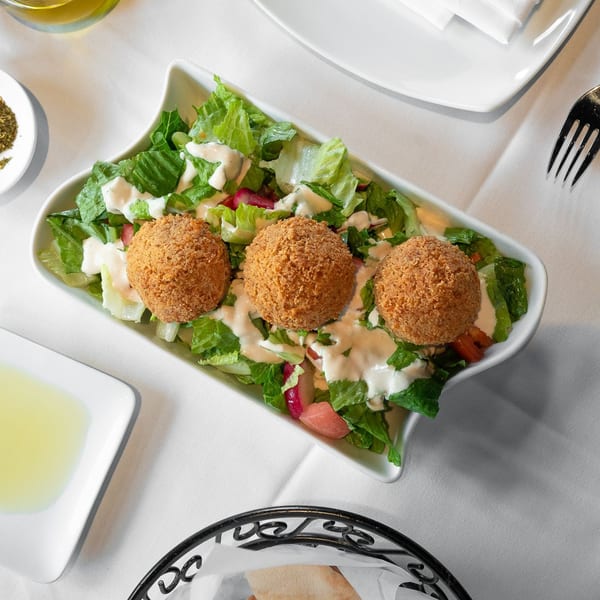 Three golden-brown falafel balls rest on a bed of fresh green lettuce with creamy dressing.