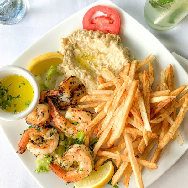 Grilled shrimp with fries, hummus, lemon, and a tomato slice on a white plate at Leila Restaurant.