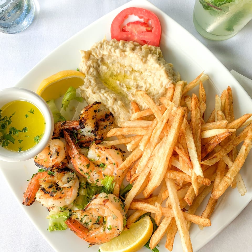 Grilled shrimp with fries, hummus, lemon, and a tomato slice on a white plate at Leila Restaurant.