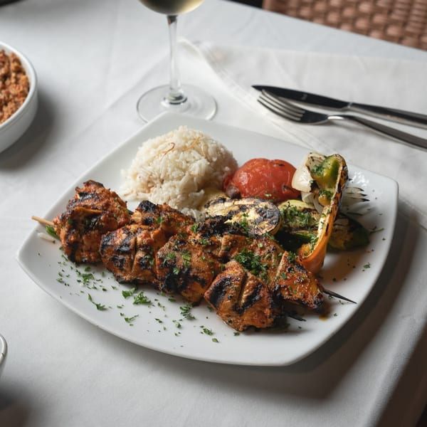 Leila Restaurant's chicken shish tawook with rice, grilled vegetables, and a glass of white wine.