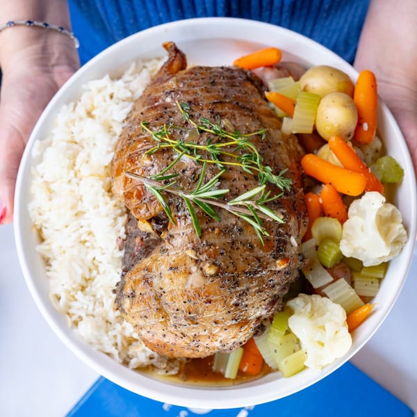 Hands holding a white bowl of Leila Restaurant's roasted meat, rice, and mixed vegetables.