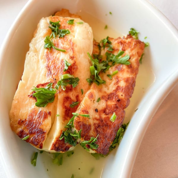 Two pieces of golden-brown fried halloumi cheese with parsley in a white dish with oil.