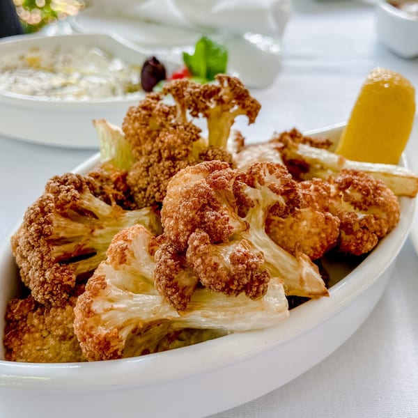 Crispy fried cauliflower florets with a lemon wedge in a white bowl at Leila Restaurant.