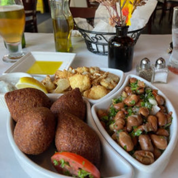 Middle-Eastern dishes including kibbeh, fried cauliflower, and foul mudammas on a white table.