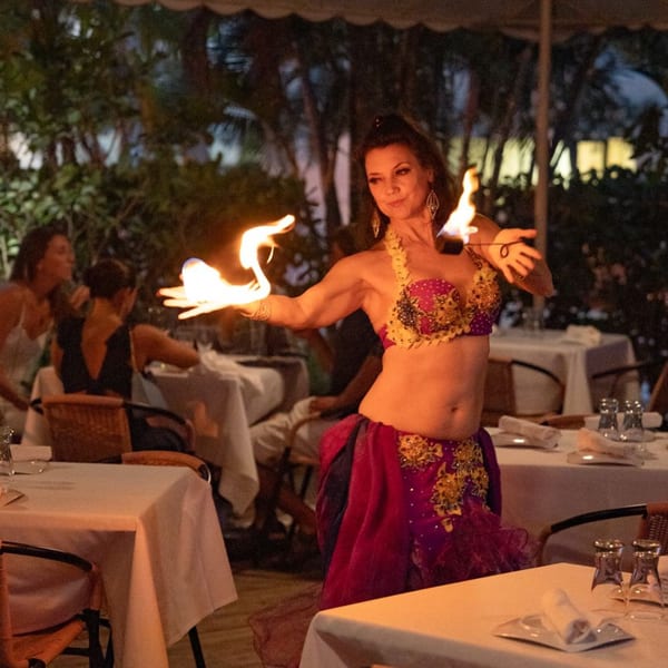 A belly dancer in a vibrant costume performs with fire at Leila Restaurant, entertaining guests at outdoor tables.